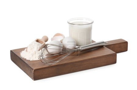 Board with metal whisk, raw eggs, flour, milk and scoop isolated on white