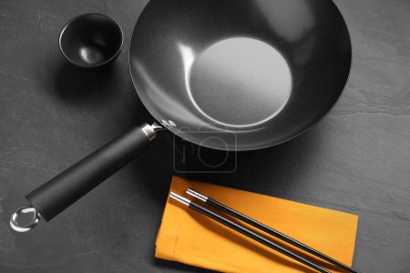 Photo for Empty iron wok, sauce bowl and chopsticks on black table - Royalty Free Image