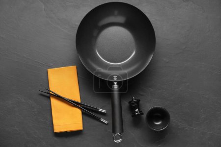 Photo for Empty iron wok, sauce bowl and chopsticks on black table, flat lay - Royalty Free Image