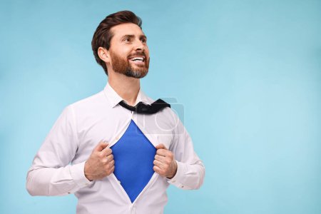 Foto de Feliz hombre de negocios con traje de superhéroe bajo traje sobre fondo azul claro. Espacio para texto - Imagen libre de derechos