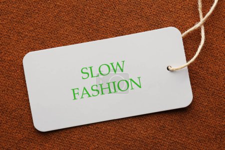 Bewusster Konsum. Tag mit Schriftzug Slow Fashion auf braunem Stoff, Draufsicht
