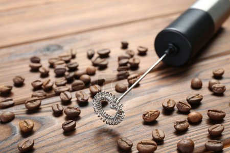 Black milk frother wand and coffee beans on wooden table, closeup