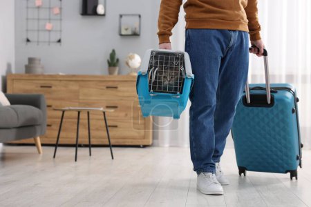 Reisen mit Haustier. Mann mit Tragetasche mit niedlicher Katze und Koffer zu Hause, Nahaufnahme. Raum für Text
