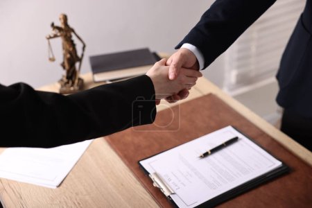 Photo for Notary shaking hands with client at wooden table in office, closeup - Royalty Free Image