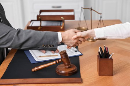 Notary shaking hands with client at wooden table in office, closeup