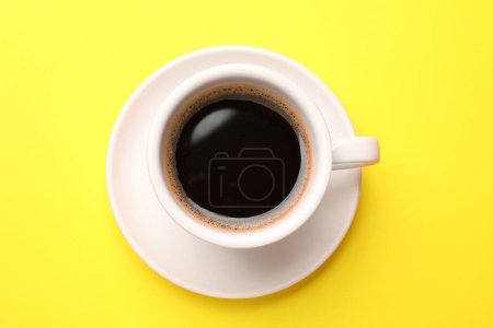 Foto de Café fresco en taza sobre fondo amarillo, vista superior - Imagen libre de derechos