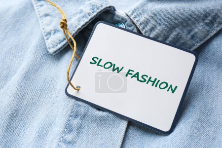 Conscious consumption. Tag with words Slow Fashion on denim shirt, closeup