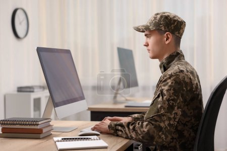 Military service. Young soldier working with computer at wooden table in office