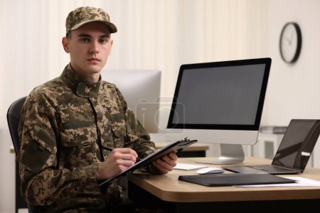 Military service. Young soldier with clipboard working at table in office