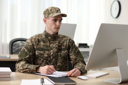Military service. Young soldier working at wooden table in office