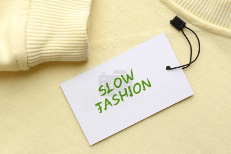 Bewusster Konsum. Tag mit Schriftzug Slow Fashion auf gelbem Sweatshirt, Draufsicht