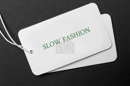 Bewusster Konsum. Tag mit Wörtern Slow Fashion auf schwarzem Hintergrund, Draufsicht