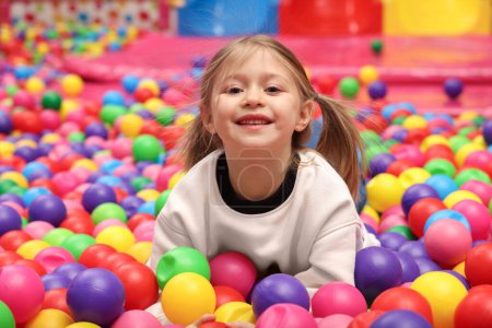 Bonne petite fille couchée sur des boules colorées dans la fosse à boules