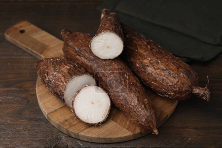 Téléchargez les photos : Racines de manioc entières et coupées sur table en bois - en image libre de droit