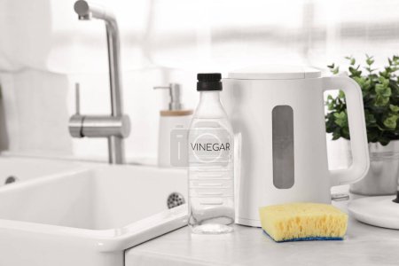 Cleaning electric kettle. Bottle of vinegar and sponge on countertop in kitchen