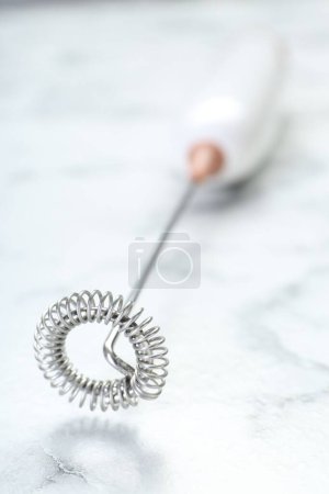 Milk frother wand on white marble table, closeup