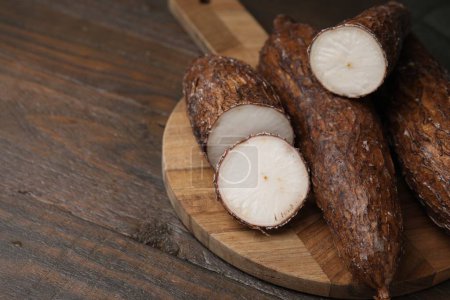 Téléchargez les photos : Racines de manioc entières et coupées sur table en bois, gros plan. Espace pour le texte - en image libre de droit