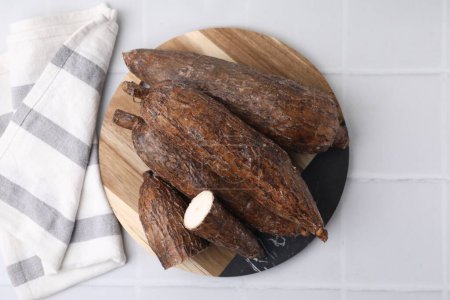Téléchargez les photos : Racines de manioc entières et coupées sur table carrelée blanche, vue du dessus - en image libre de droit