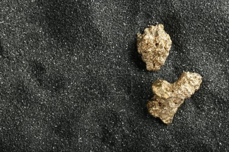 Photo for Shiny gold nuggets on black sand, top view. Space for text - Royalty Free Image