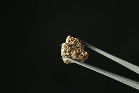 Photo for Tweezers with gold nugget against black background, closeup. Space for text - Royalty Free Image