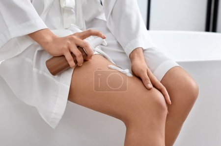 Foto de Mujer aplicando producto auto-bronceado en su pierna en la bañera en el baño, primer plano - Imagen libre de derechos