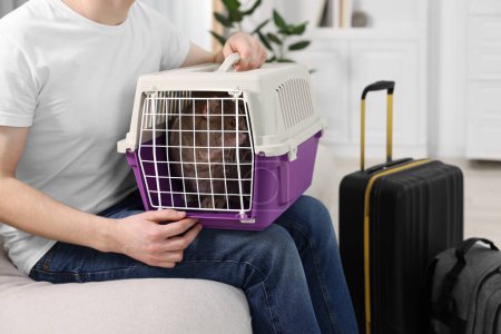 Téléchargez les photos : Voyage avec animal de compagnie. Homme tenant transporteur avec chat mignon sur le canapé à la maison, gros plan - en image libre de droit