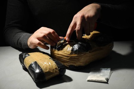 Foto de Contrabando y tráfico de drogas. Hombre abriendo paquete de narcóticos con cortadora de cajas en la oscuridad, primer plano - Imagen libre de derechos