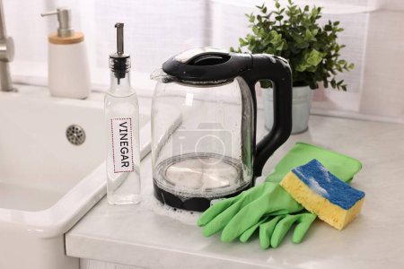 Cleaning electric kettle. Bottle of vinegar, rubber gloves and sponge with foam on countertop in kitchen