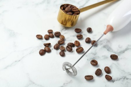 Milk frother wand and coffee beans on white marble table, closeup. Space for text
