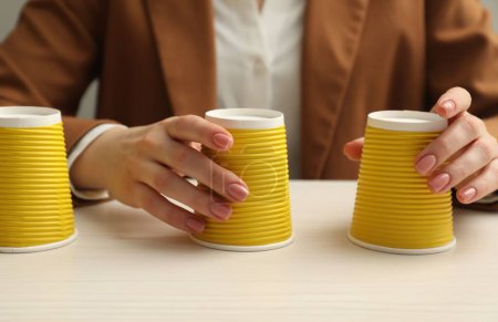 Woman playing shell game with yellow cups at white wooden table, closeup