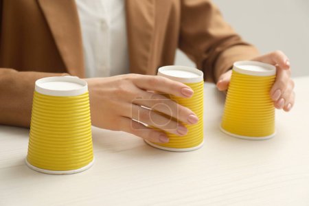 Téléchargez les photos : Femme jouant jeu de coquille avec des tasses jaunes à la table en bois blanc, gros plan - en image libre de droit
