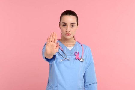 Mamólogo con cinta rosa mostrando gesto de stop sobre fondo de color. Concientización sobre el cáncer de mama