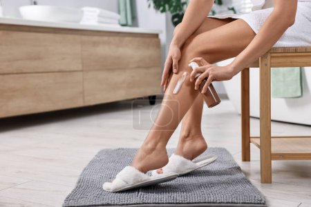 Foto de Mujer aplicando producto auto-bronceado en la pierna en silla de madera en el baño, primer plano. Espacio para texto - Imagen libre de derechos