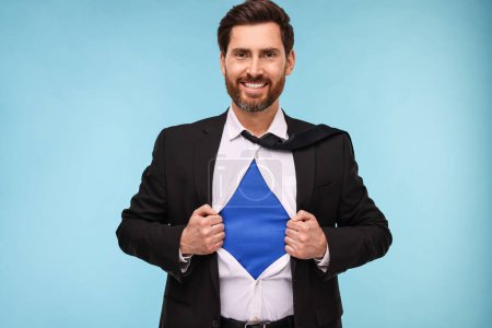 Foto de Feliz hombre de negocios con traje de superhéroe bajo traje sobre fondo azul claro - Imagen libre de derechos