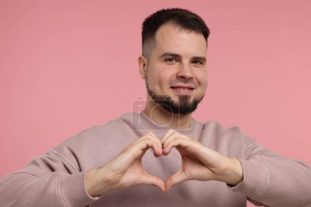 Mann zeigt Herz-Geste mit Händen auf rosa Hintergrund