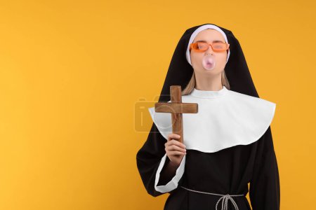 Woman in nun habit and sunglasses blowing bubble gum against orange background. Space for text