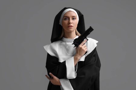 Mujer en hábito monja sosteniendo pistola sobre fondo gris
