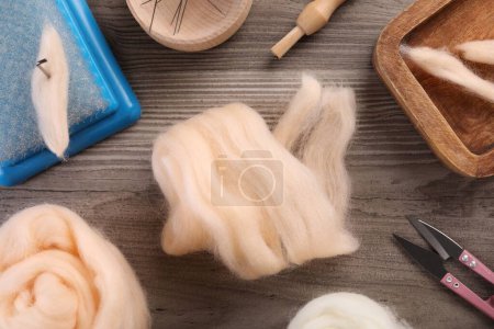 Felting wool and different tools on wooden table, flat lay