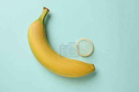 Téléchargez les photos : Banane et préservatif sur fond turquoise, plat. Concept de sexe sûr - en image libre de droit