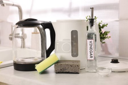 Cleaning electric kettle. Bottle of vinegar, sponges and baking soda on countertop in kitchen