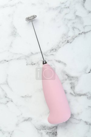 Pink milk frother wand on white marble table, top view