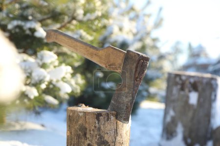 Metal axe in wooden log outdoors on sunny winter day, closeup