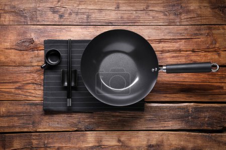 Photo for Empty iron wok, sauce bowl and chopsticks on wooden table, flat lay - Royalty Free Image