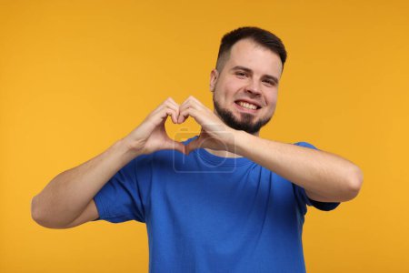 Mann zeigt Herz-Geste mit Händen auf goldenem Hintergrund