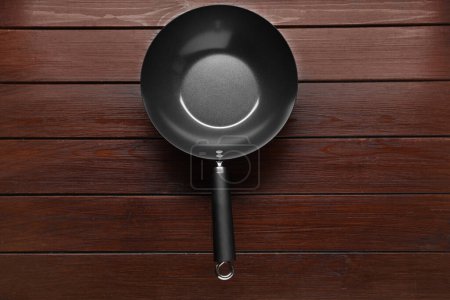 Empty iron wok on dark wooden table, top view. Chinese cookware