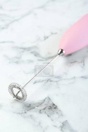 Pink milk frother wand on white marble table, closeup