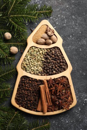 Different spices, nuts and fir branches on dark gray textured table, flat lay