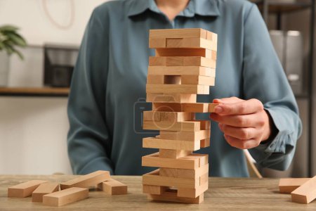 Playing Jenga. Woman removing block from tower at wooden table indoors, closeup