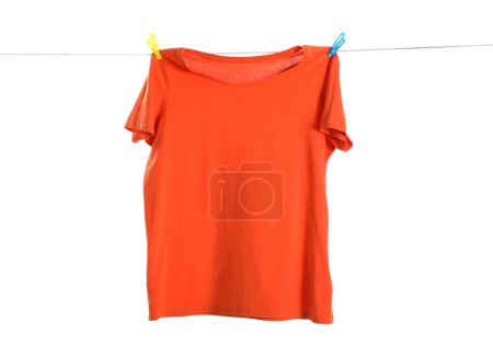 Un t-shirt orange séchant sur la ligne de lavage isolé sur blanc