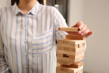 Playing Jenga. Woman building tower with wooden blocks indoors, closeup